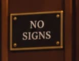 The no signs plaque. This invented wall fixture makes the raised sign a visual joke about the room's rules. It is illustrative staging, not a claim that this plaque hung at the hearing.