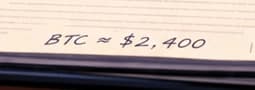 The rounded price note. BTC approximately $2,400 evokes a reported price that afternoon. The amount is rounded for the illustration and does not establish Bitcoin's price at the instant the sign appeared.