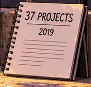 THE IMPACT NOTEBOOK. 37 PROJECTS recalls The Water Project's impact account. The 2019 notation signals the later reporting context; it does not date all 37 completions to 2018 or identify this fictional scene as a documented visit.