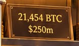21,454 BTC / $250m. The plate records the announced purchase. The $250 million total includes fees and expenses; the gold stacks are a visual metaphor, not a literal inventory of physical bitcoins.