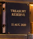 THE TREASURY FOLDER. TREASURY RESERVE and 11 AUG 2020 tie the folder to the policy announcement. This fictional prop anchors the scene to a dated corporate decision.