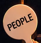 THE PEOPLE PADDLE. The foreground paddle reads PEOPLE, matching ConstitutionDAO's contribution token. Lowered in the bidder's hand, this invented prop stands for the many individual contributors behind the attempt. It is not an authentic paddle used at Sotheby's.